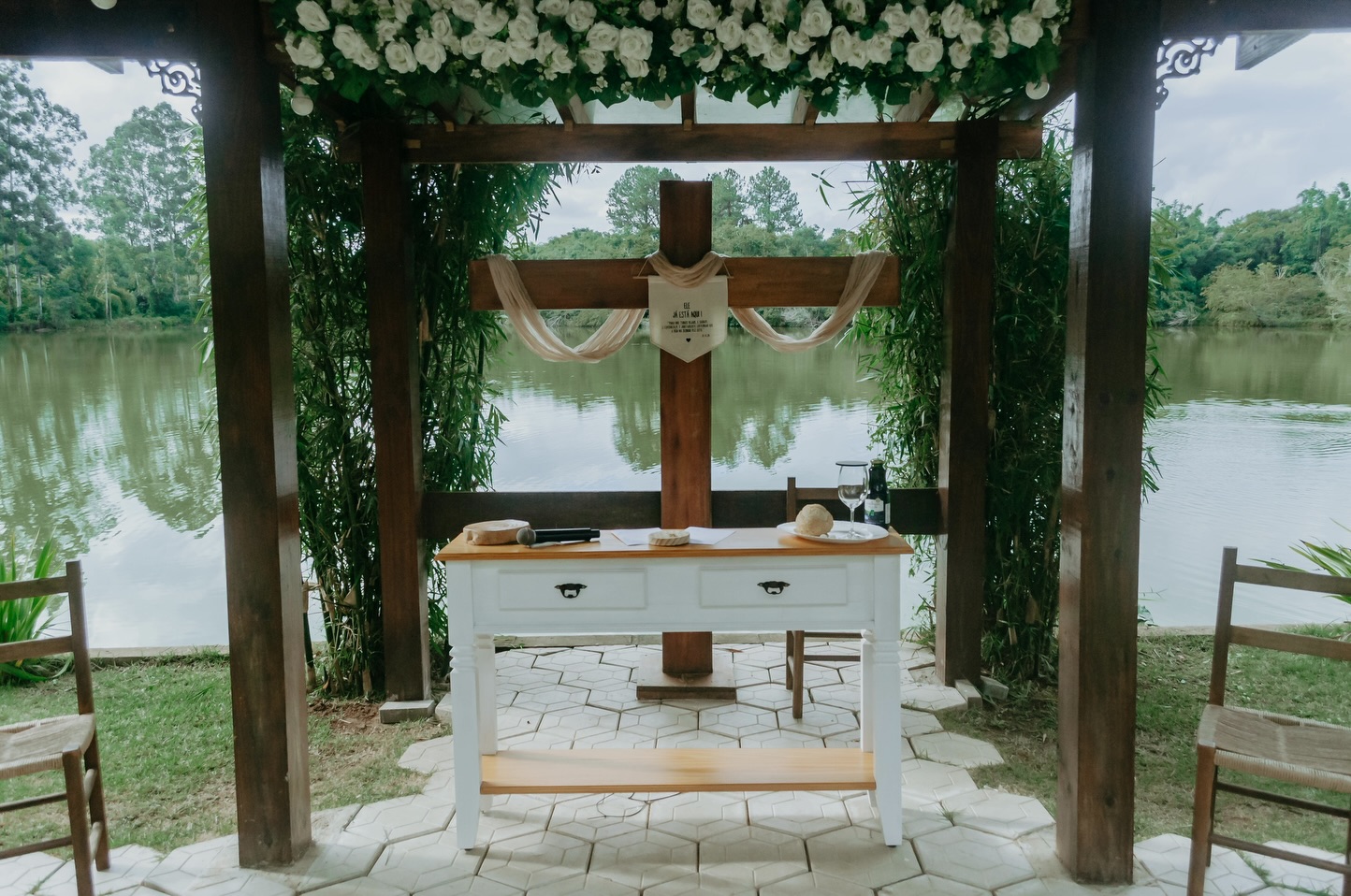 Altar com cruz sob pérgola florida diante do lago